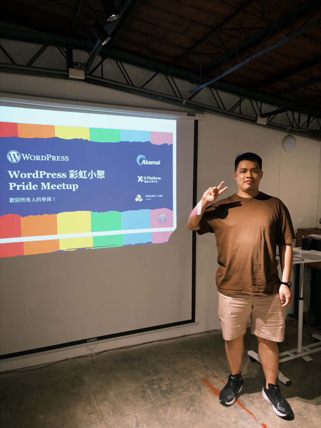講者 Moksa 站在「WordPress 彩虹小聚 Pride Meetup 歡迎所有人的參與!」的開場投影片旁比 YA(照片來源:WordPress 彩虹小聚 LINE 群組)