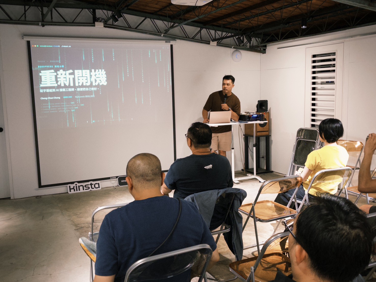 Moksa 在台上分享,投影幕上是〈重新開機〉的標題投影片,副標寫著「從字幕組到 AI 接案工程師,順便把自己修好。」(照片來源:WordPress 彩虹小聚 LINE 群組)